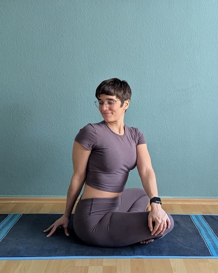 Clémence assise en tailleur sur son tapis, dans une pièce ordinaire, le regard baissé et le sourire calme.