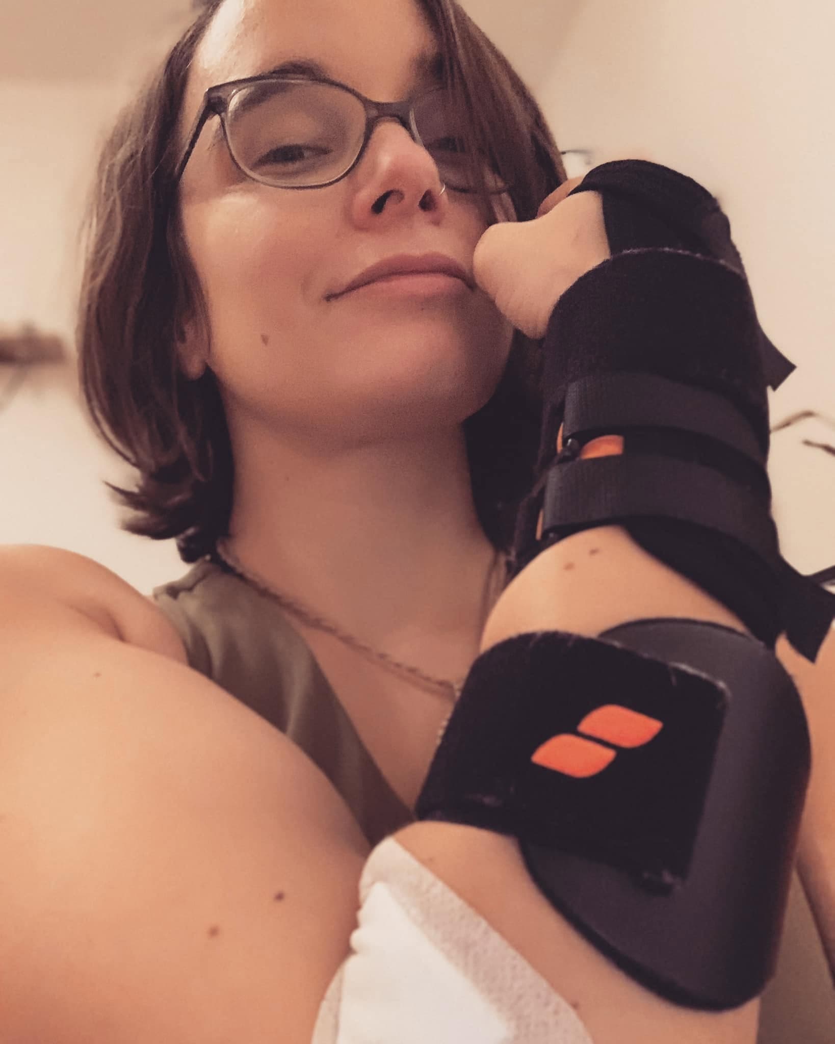 Clémence, le poignet immobilisé dans une attelle noire, la tête posée contre sa main.