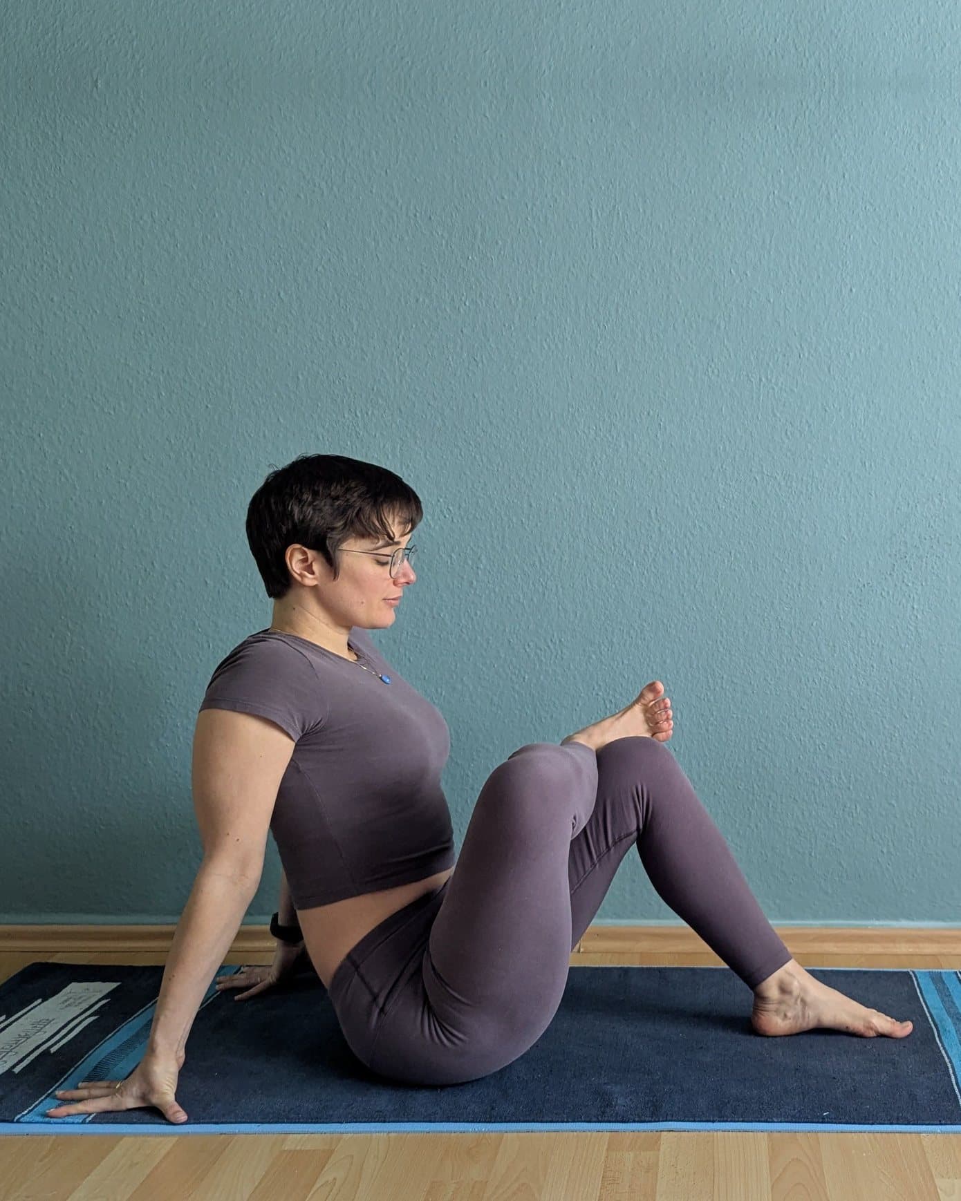 Clem sitting on her mat, leaning back on her hands, one ankle resting on the opposite knee to open the hip.