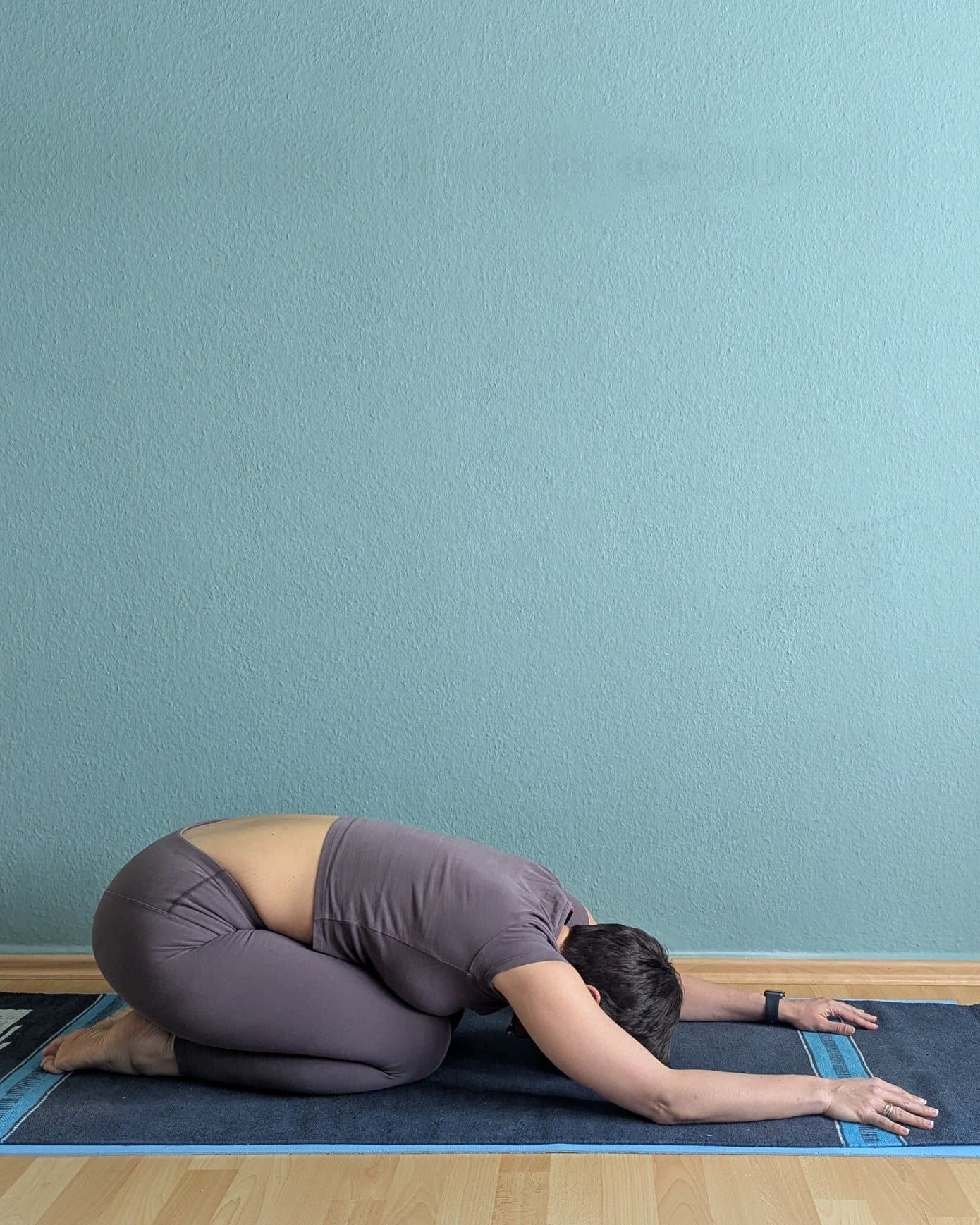 Clem in child’s pose on her mat, forehead towards the floor and arms stretched out in front of her.